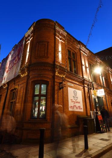 Image of the outside of Tiny Rebel at night, which is a red bricked building on the corner of the street