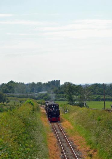 A narrow gauge train with a town and sea in the background.