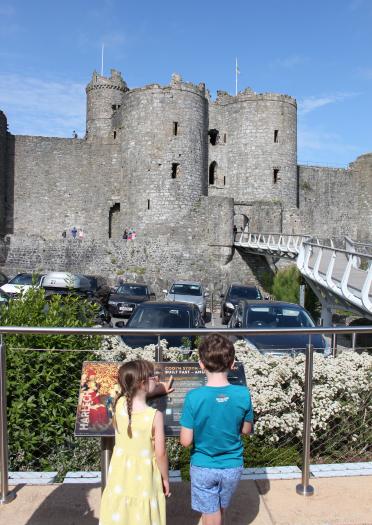 Zwei Kinder stehen an einer Infotafel vor einer Burg.
