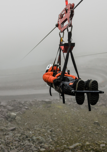 Person mit Helm, gesichert an einer Zipline über einem Schiefersteinbruch.