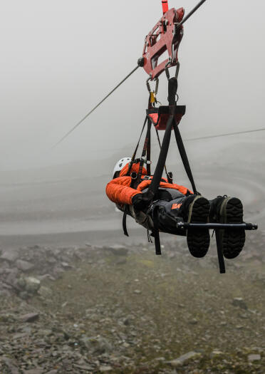 Person wearing a hard hat and safety harness riding a zip line, suspended over a slate quarry.