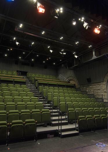 Innenraum eines Theaters mit grünen Sitzen, Bühne im Vordergrund.