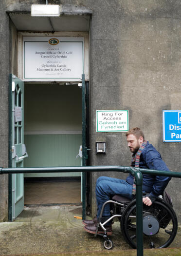 Ein Mann im Rollstuhl benutzt eine Rampe, um in ein Gebäude zu gelangen.