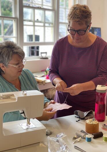 woman stood looking at sewing and woman sat at sewing machine.