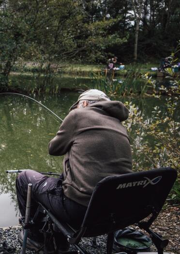 man sat fishing at edge of lake.