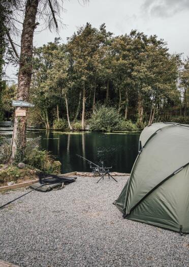 Fishing tent and equipment near edge of lake.