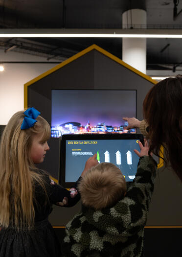 Two children and an adult interacting with a display screen.
