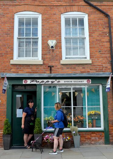 two women and a dog outside red brick florist shop 'Poppy's'.