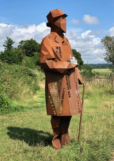 A tall rusty metal sculpture of a man in a field.