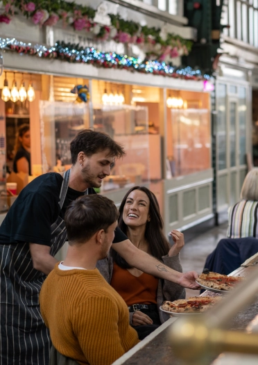 A couple eating pizza in an indoor market.
