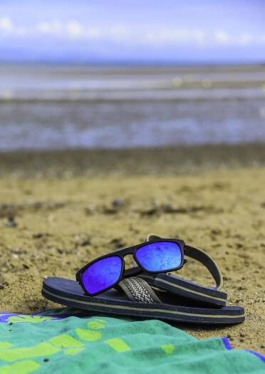 Flip flops and sunglasses on a beach towel, on a sandy beach.