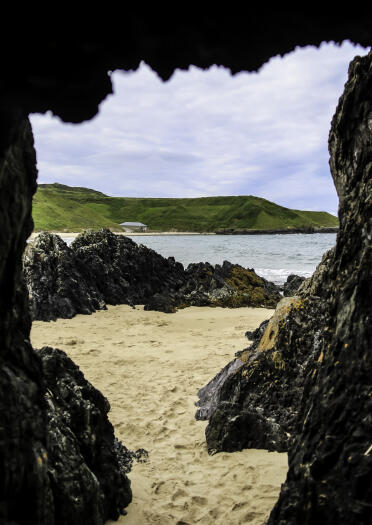 Looking out onto a sandy beach from a cave mouth.