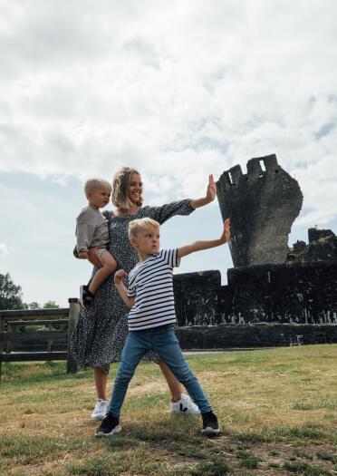 A woman and two children pretending to hold up a leaning castle tower.