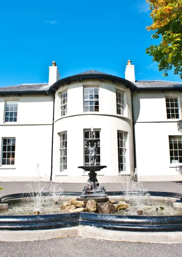 A white painted Regency house with a fountain in front.