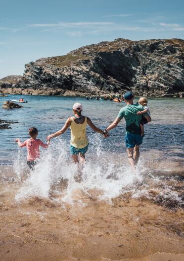Two adults and two young children running into the sea.
