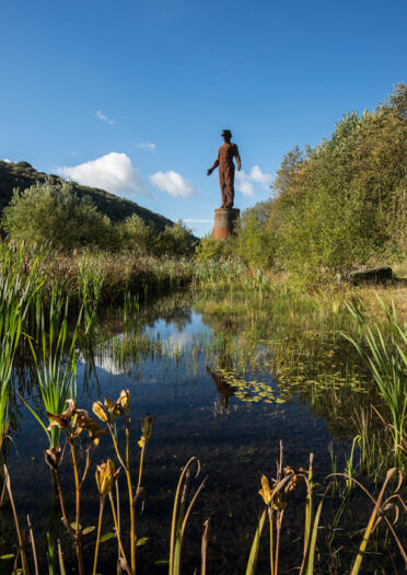 Eine verwitterte Skulptur eines Mannes an einem Teich.