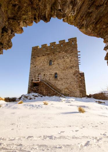 A square castle tower in the snow, viewed through a stone archway.