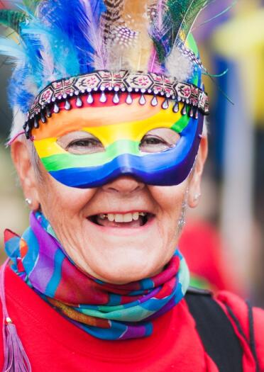 Smiling woman wearing rainbow mask and feathered headdress
