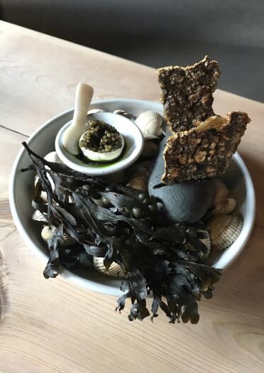 A bowl of seaweed and shells, with a tiny bowl of caviar on top.
