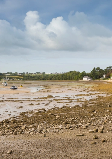 A pebbly beach with boats moored in the water.