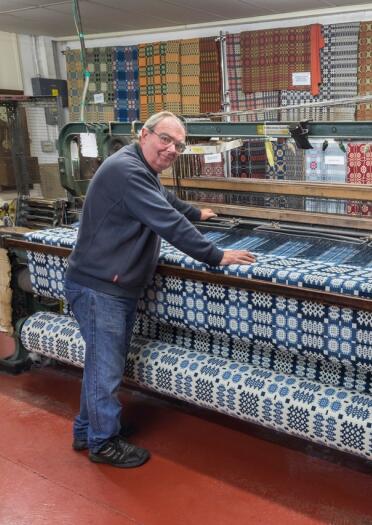 A weaver working on a weaving Ein Weber arbeitet an einem Webstuhl und stellt traditionelle walisische geometrische, bunte Stoffe her. loom making traditional Welsh geometric colourful fabrics 