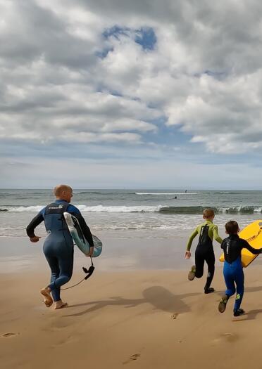 man and two boys run into sea with surfboards.
