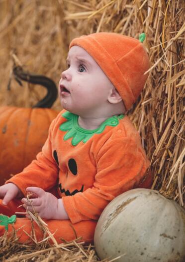 baby in pumpkin outfit with pumpkins and bales of hay.