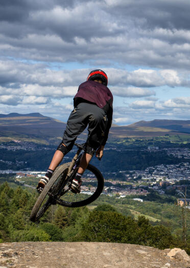 A mountain bike rider on a jump overlooking a large town.