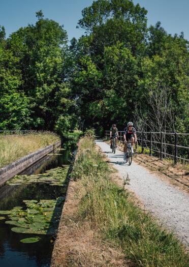 Two cyclists on a cycle path alongside a countryside canal. 