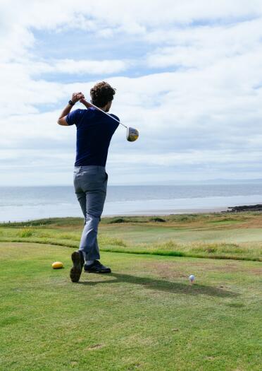 A man teeing off on a green overlooking the coast.