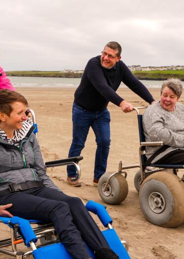 two people in beach wheelchairs and people pushing them.