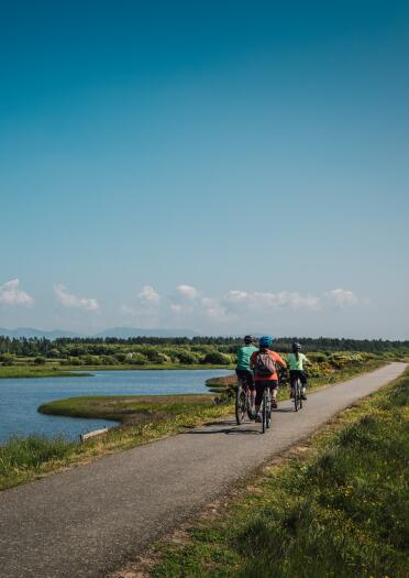 A woman and two children on a flat cycle path by a lake.
