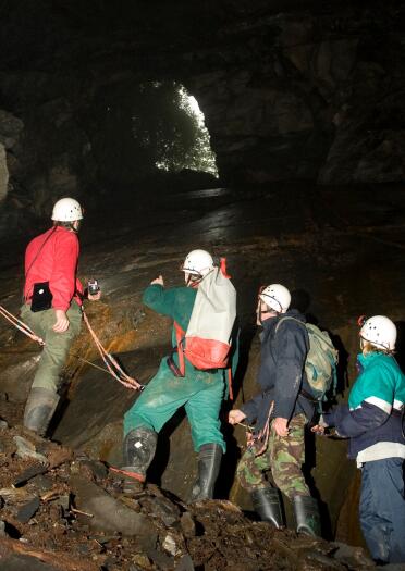 people with hard hats with lights on exploring mine with shaft of light coming through and rope being held.