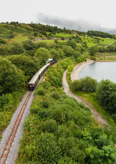 A narrow gauge steam hauled train next to a reservoir.