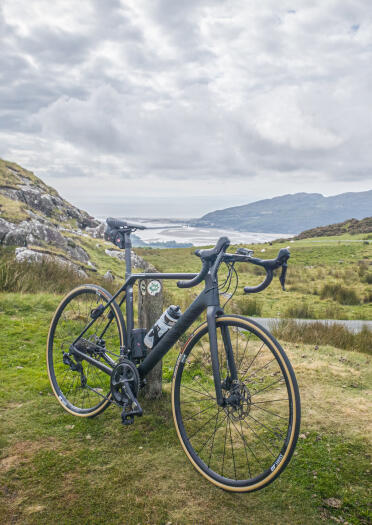 A road bike resting against a post, with estuary and mountain views in the background.