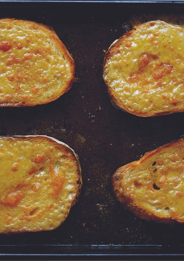 Tair tafell o rarebit Cymreig ar hambwrdd du.
