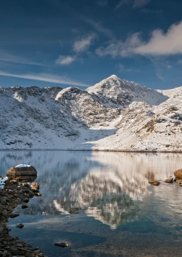 Walker looking towards snow-covered summit of Snowdon (Yr Wyddfa) from Llyn Llydaw.