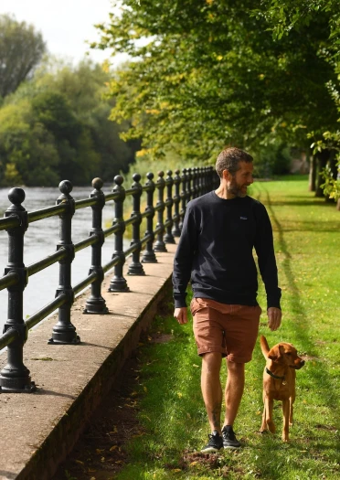 man, woman and dog walking near river, with black railing.