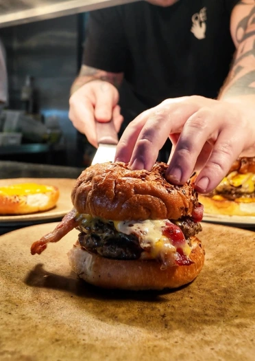 A chef putting a massive beef burger onto a plate.