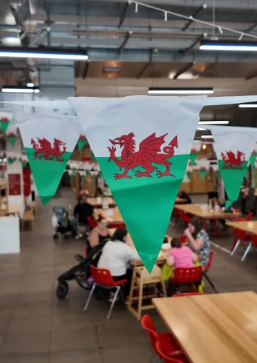 canteen area with Welsh flag bunting with people, tables and chairs.