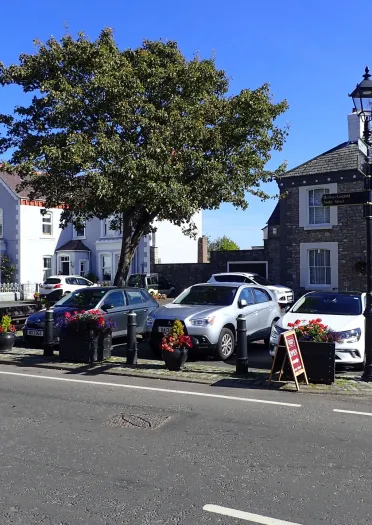 road in foreground, flower pots and bollards with parked cars in the mid ground and buildings in the background