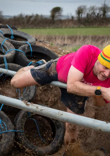 A man climbing over a bar through a muddy course