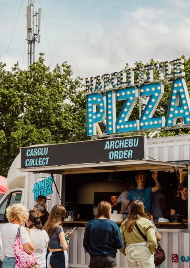 pizza food stall at National Eisteddfod with bilingual signage and people queuing.