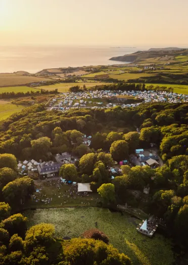 aerial view of festival, surrounding countryside and sun on sea.