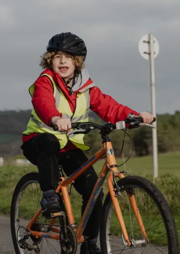 child wearing helmet on adaptive bike in country park.