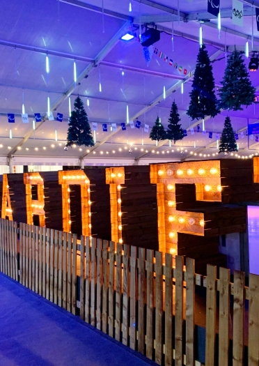 Cardiff sign lit up behind fence and Christmas trees hanging from ceiling.