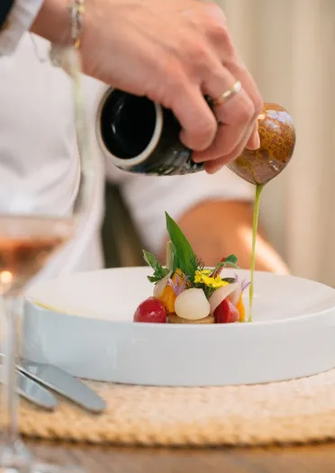 A small plate of food being drizzled with dressing at a restaurant.