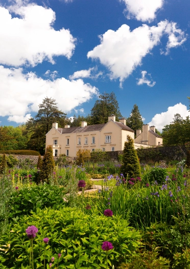 Aberglasney garden displaying flowers and shrubs with manor house in background.