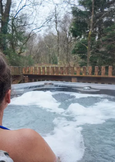 A person relaxing in an outdoor hot tub overlooking trees.