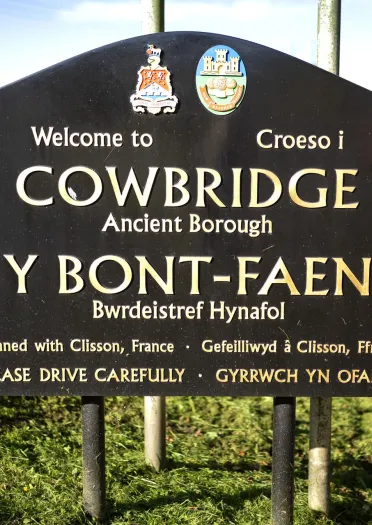 A bilingual 'Welcome to Cowbridge' sign by a roadside.